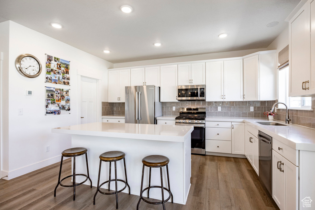 Kitchen with appliances with stainless steel finishes, a sink, a breakfast bar area, wood finished floors, and recessed lighting