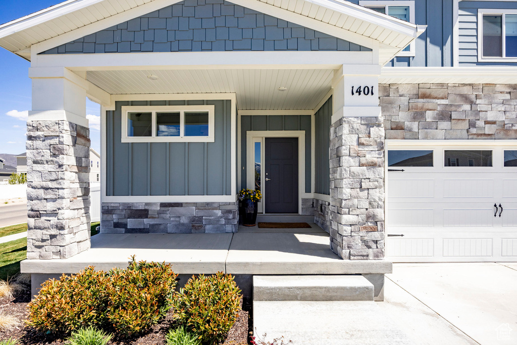 Entrance to property with board and batten siding, covered porch, stone siding, and a garage
