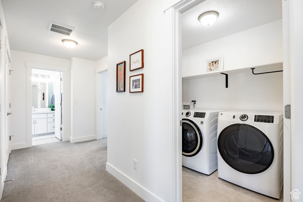 Laundry room featuring washer and clothes dryer, baseboards, and light colored carpet