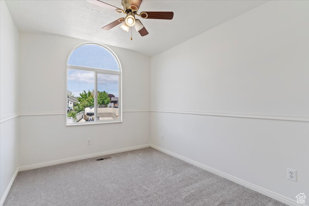 Carpeted spare room featuring ceiling fan and baseboards