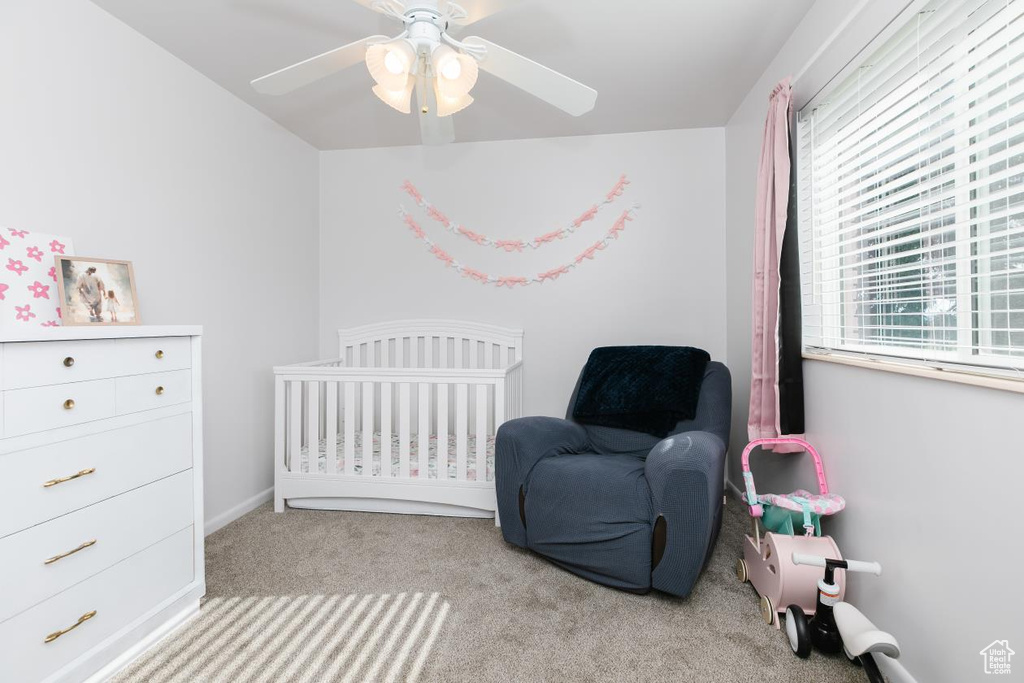 Carpeted bedroom featuring a crib and ceiling fan