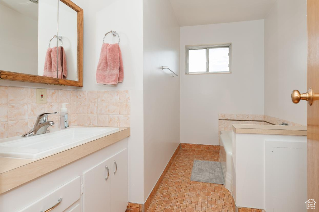Full bathroom featuring vanity, backsplash, a garden tub, and baseboards