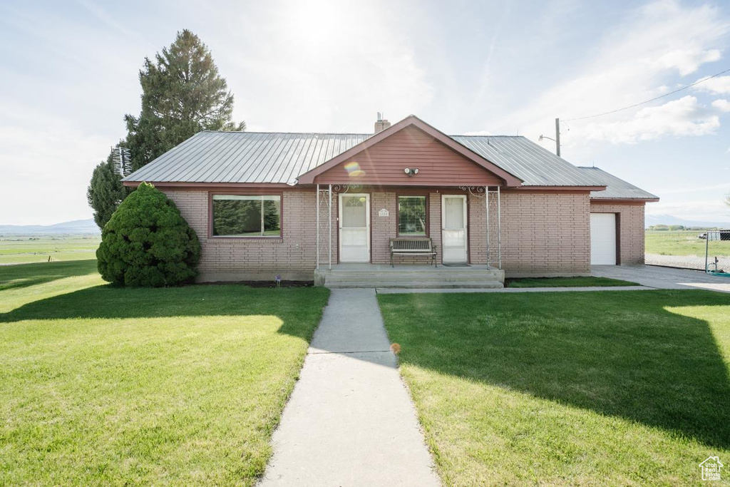 View of front of home featuring covered porch, a garage, a front lawn, and brick siding