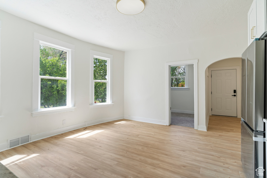 Empty room featuring plenty of natural light, visible vents, arched walkways, and light wood-type flooring