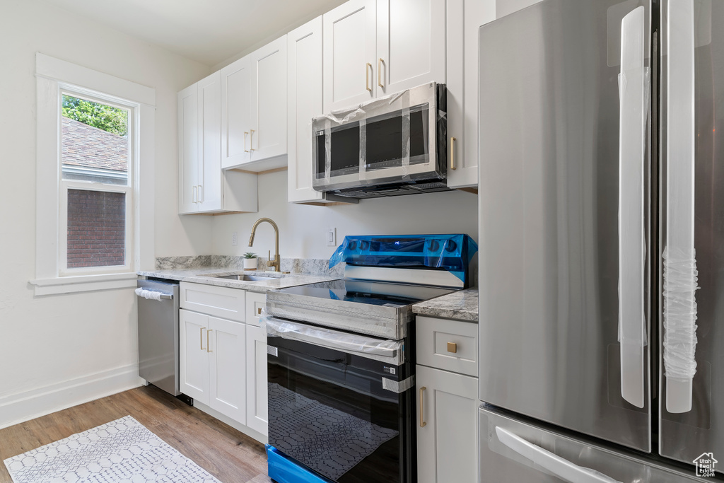 Kitchen featuring a sink, stainless steel appliances, white cabinets, baseboards, and light wood-style floors
