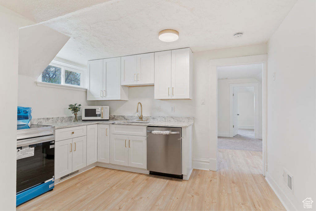Kitchen with light wood finished floors, a sink, stainless steel appliances, white cabinets, and visible vents