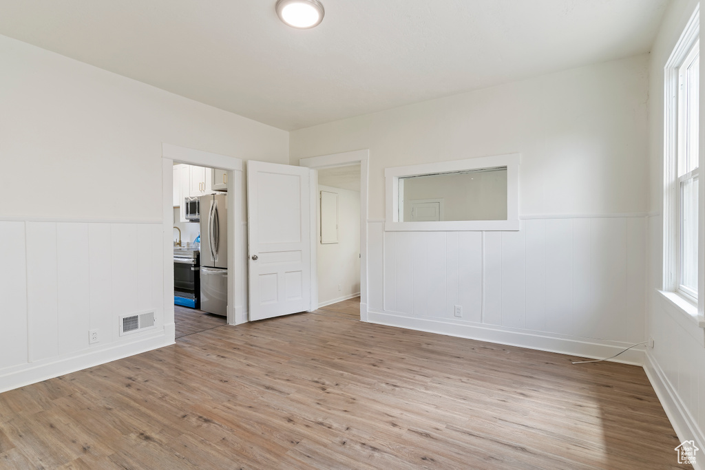 Unfurnished bedroom with freestanding refrigerator, visible vents, wainscoting, and light wood-type flooring