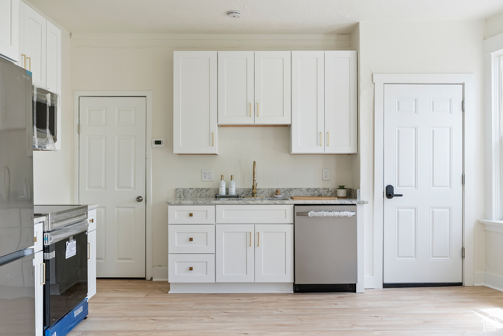 Kitchen with a sink, light wood-type flooring, white cabinets, and appliances with stainless steel finishes