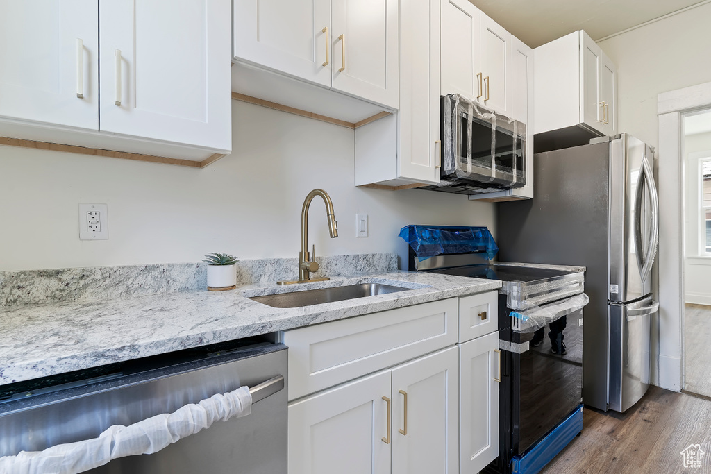 Kitchen featuring wood finished floors, a sink, white cabinetry, appliances with stainless steel finishes, and light stone counters