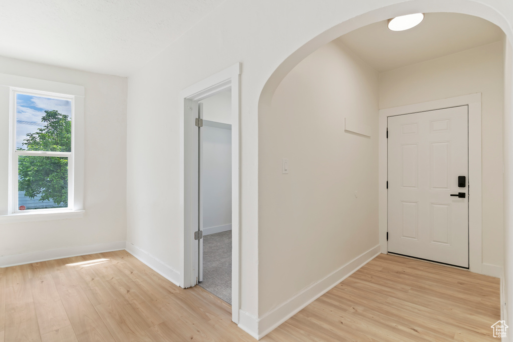 Corridor with arched walkways, light wood-style floors, and baseboards
