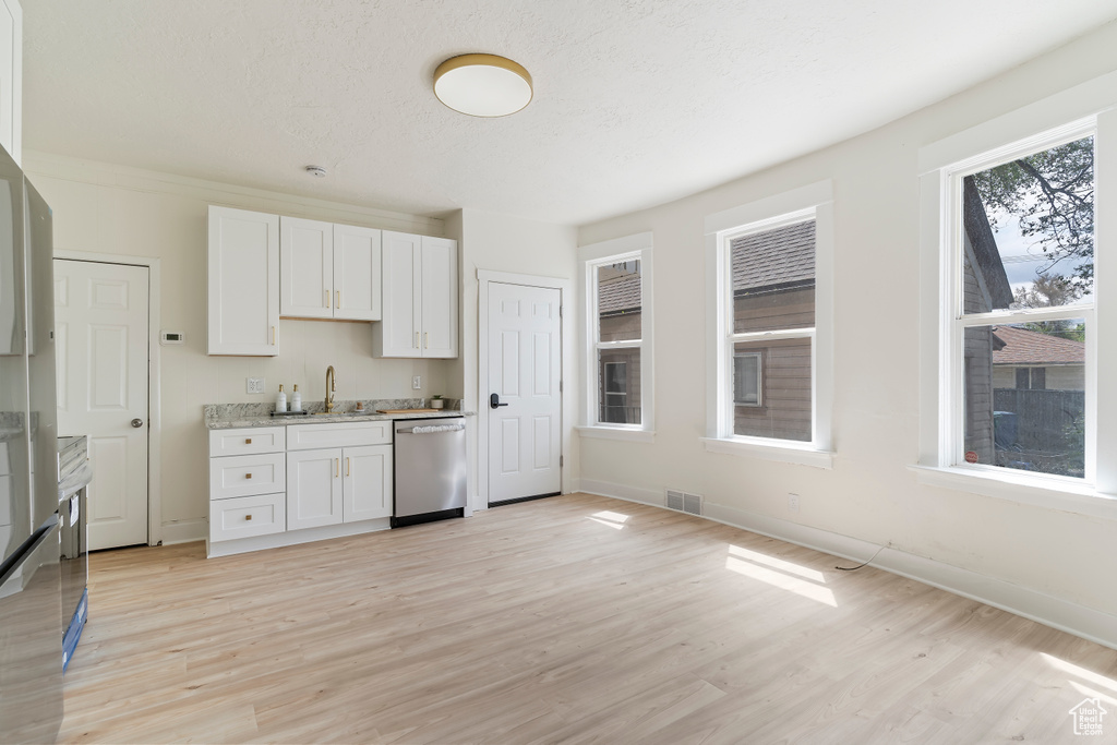 Kitchen with light wood-style flooring, white cabinetry, visible vents, baseboards, and dishwasher