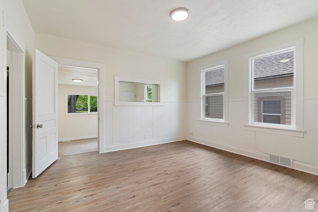 Empty room featuring wainscoting, visible vents, and light wood-style floors