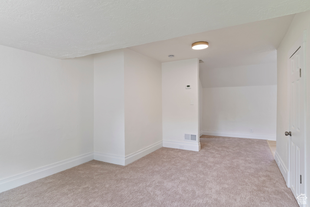 Bonus room with a textured ceiling, baseboards, visible vents, and light colored carpet