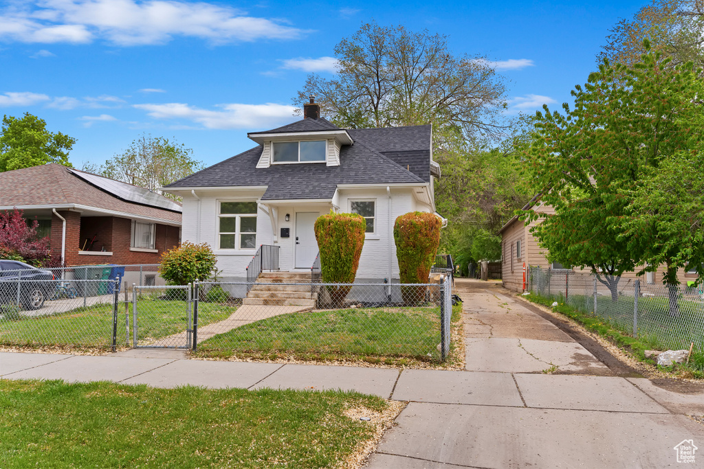 Bungalow-style home featuring a shingled roof, a fenced front yard, a front lawn, and a gate