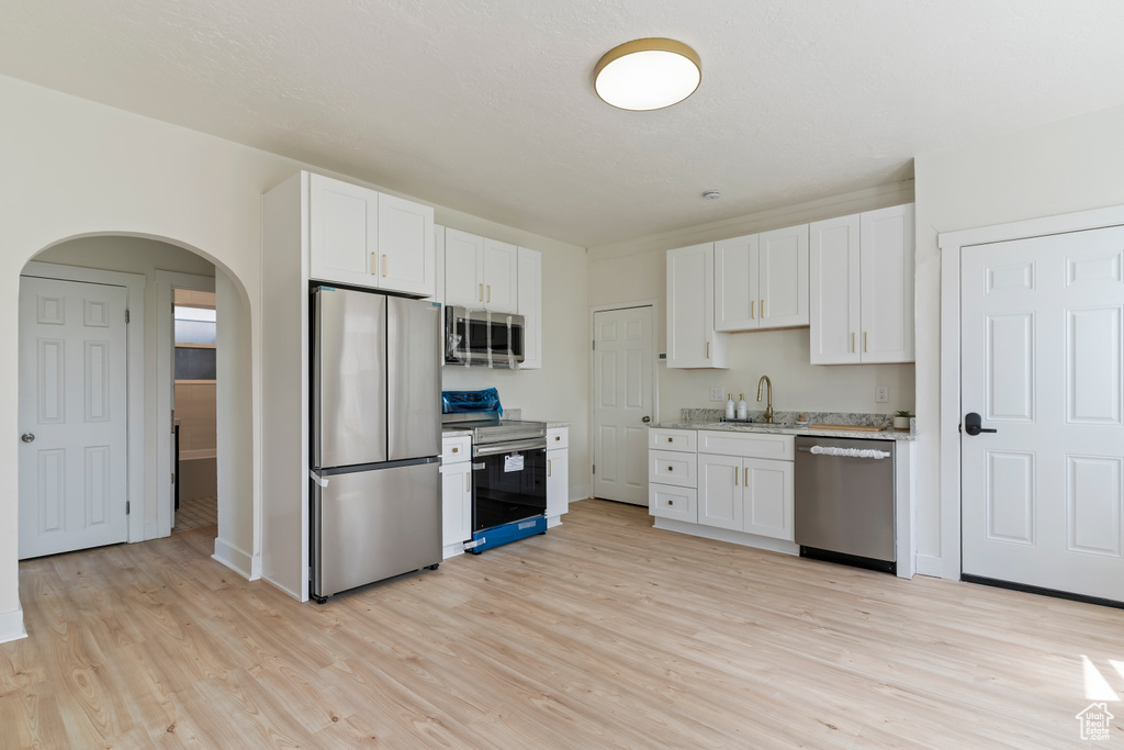 Kitchen featuring arched walkways, light wood-style floors, appliances with stainless steel finishes, and a sink