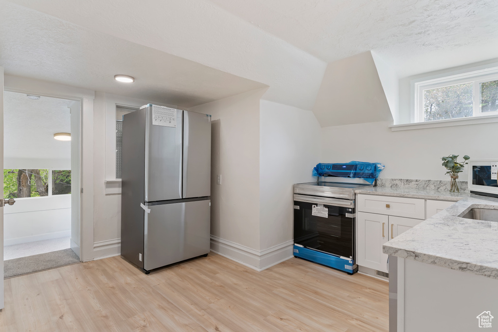 Kitchen featuring white cabinetry, stainless steel appliances, light wood-style flooring, and light stone countertops