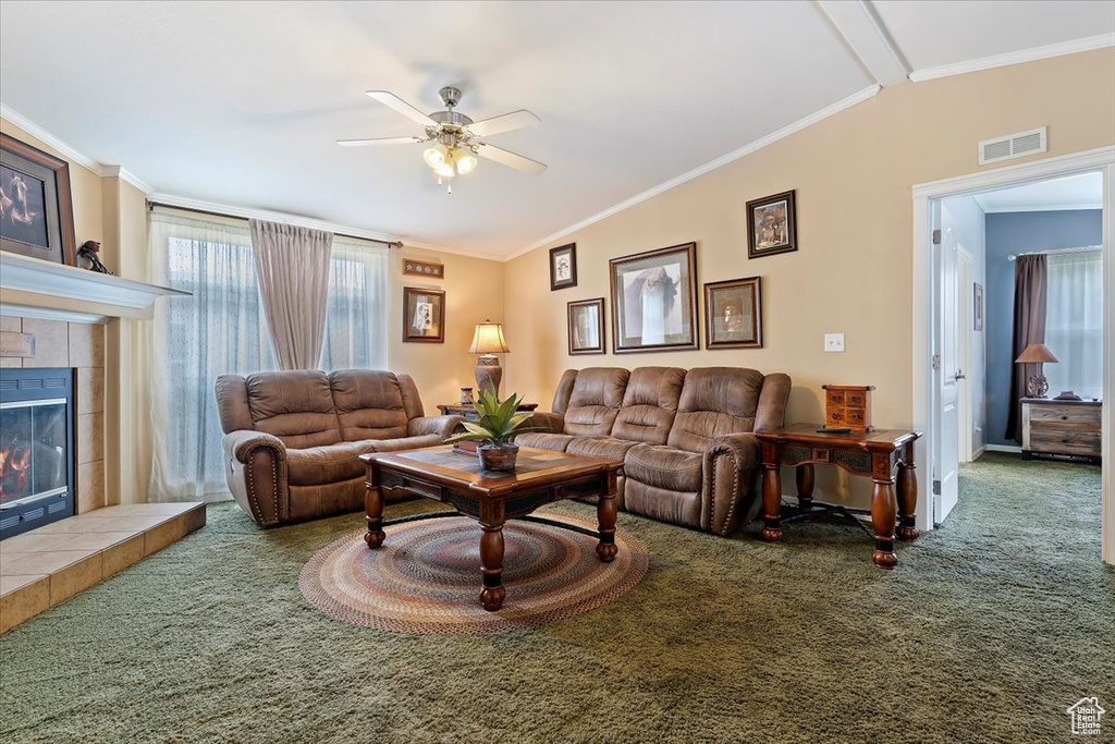 Carpeted living room featuring a tiled fireplace, crown molding, visible vents, ceiling fan, and lofted ceiling