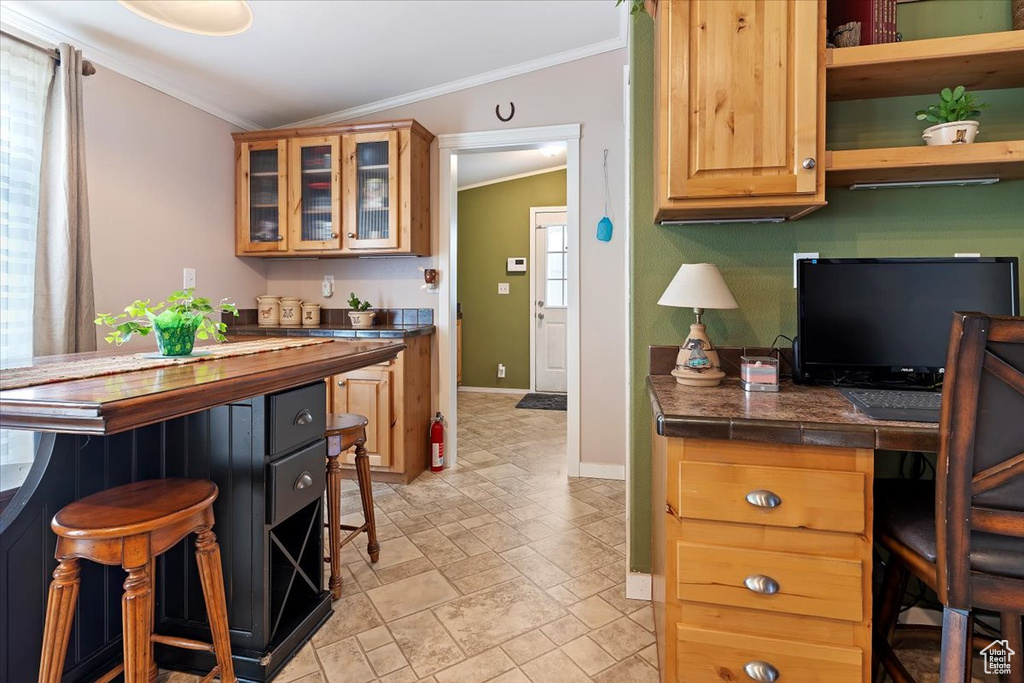 Kitchen with a breakfast bar area, glass insert cabinets, stone finish floor, crown molding, and baseboards