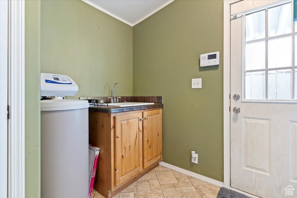 Clothes washing area with baseboards, ornamental molding, a sink, and cabinet space