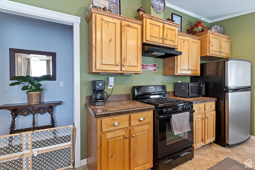 Kitchen with tile countertops, under cabinet range hood, baseboards, ornamental molding, and black appliances