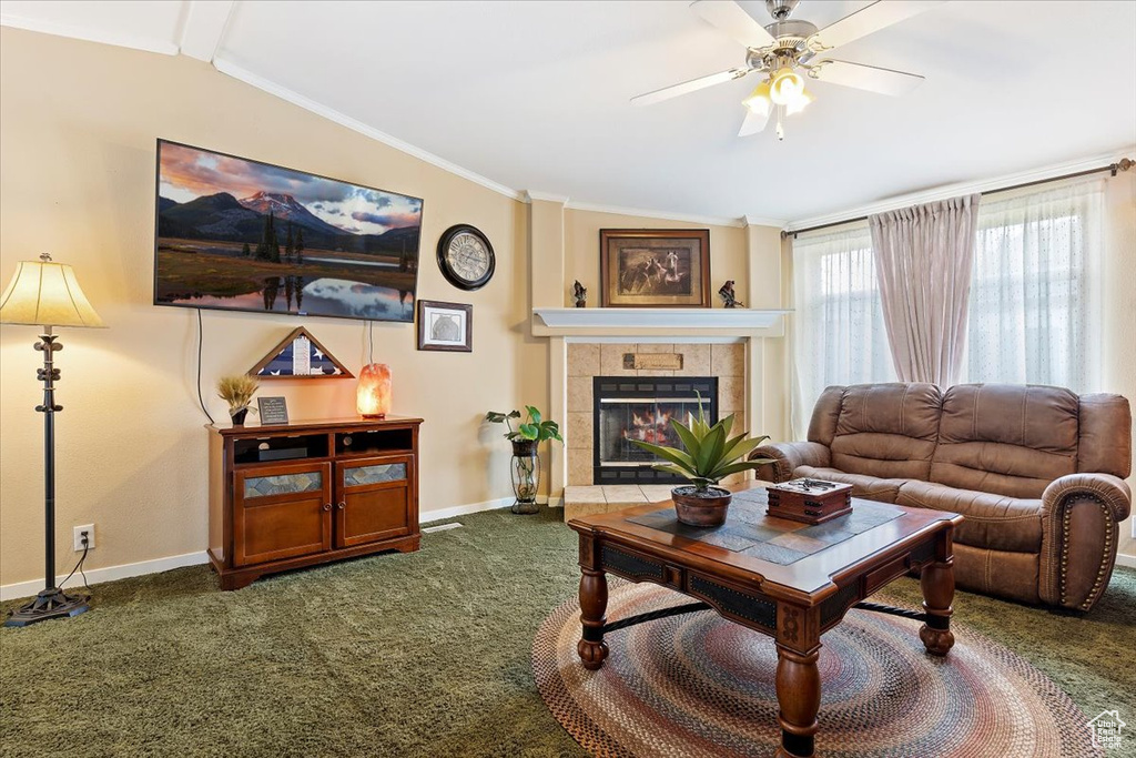 Living room featuring baseboards, ornamental molding, ceiling fan, dark carpet, and a tile fireplace