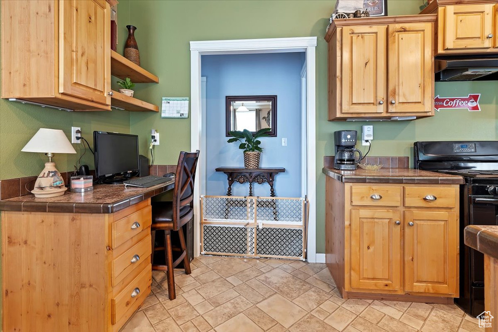 Kitchen featuring built in desk, stone finish flooring, black range with electric cooktop, under cabinet range hood, and tile countertops