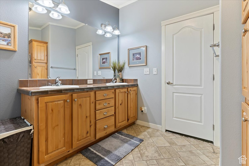 Bathroom with baseboards, crown molding, a sink, and double vanity