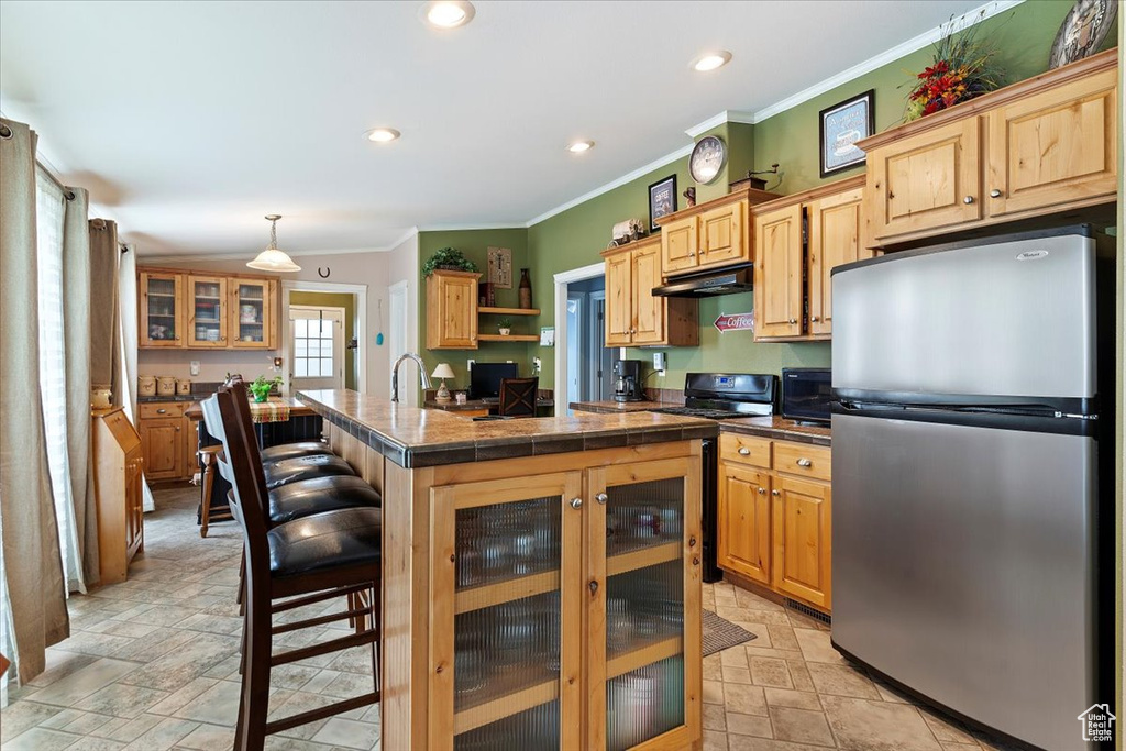 Kitchen with freestanding refrigerator, under cabinet range hood, a center island, ornamental molding, and stone finish flooring