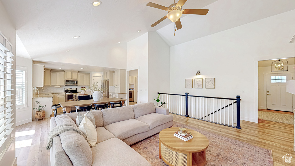 Living area with light wood-style floors, plenty of natural light, ceiling fan, a chandelier, and high vaulted ceiling