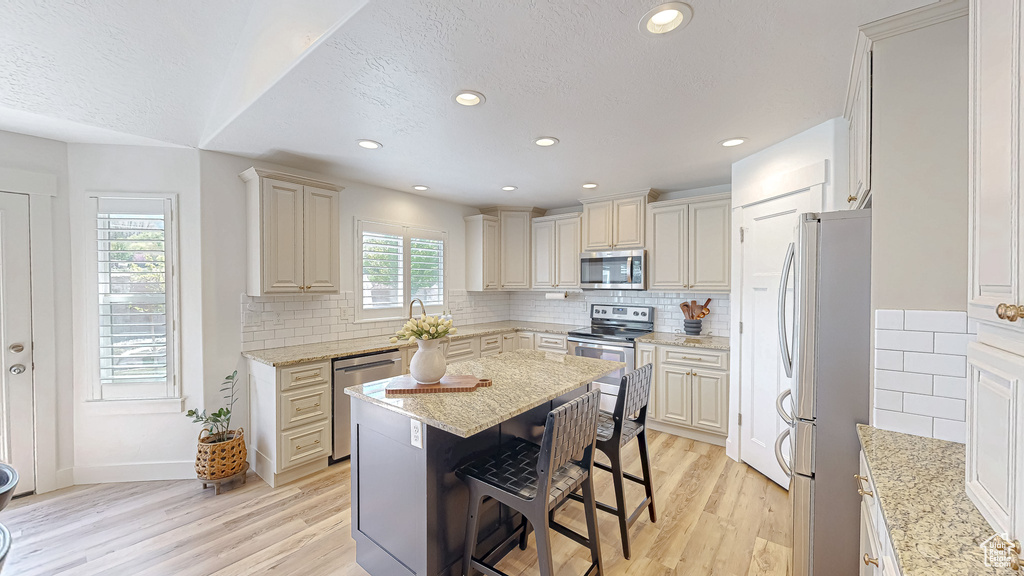 Kitchen with stainless steel appliances, a textured ceiling, light wood-style flooring, a kitchen bar, and a center island