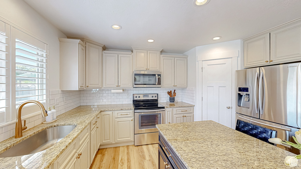 Kitchen featuring appliances with stainless steel finishes, a sink, backsplash, light wood-style flooring, and light stone counters