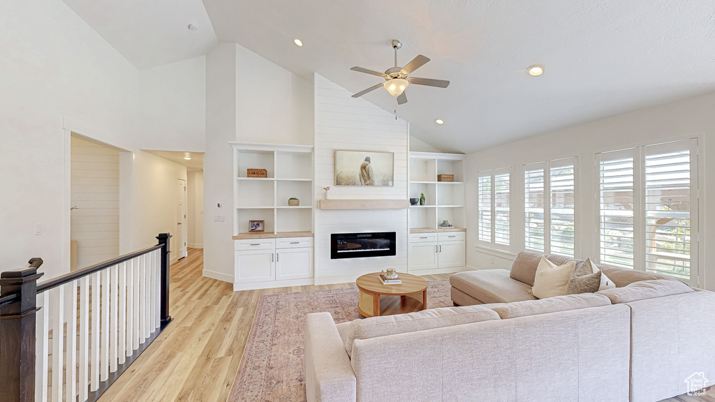 Living room featuring high vaulted ceiling, light wood-style floors, ceiling fan, a glass covered fireplace, and recessed lighting