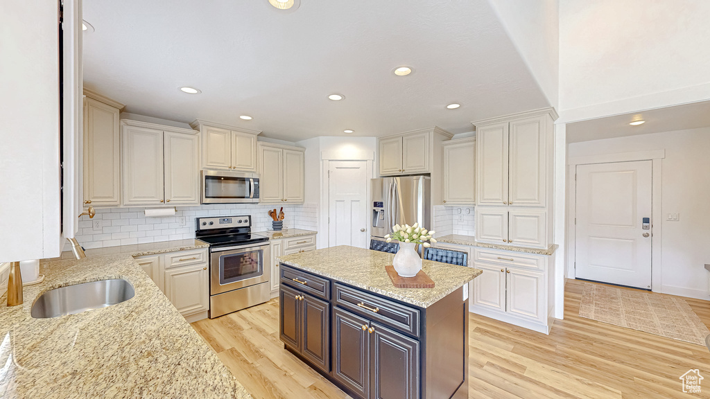Kitchen with appliances with stainless steel finishes, white cabinets, light wood-style flooring, light stone counters, and decorative backsplash