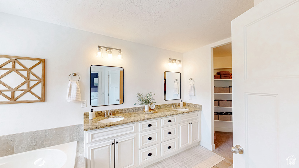 Bathroom with double vanity, a bath, a walk in closet, and a textured ceiling