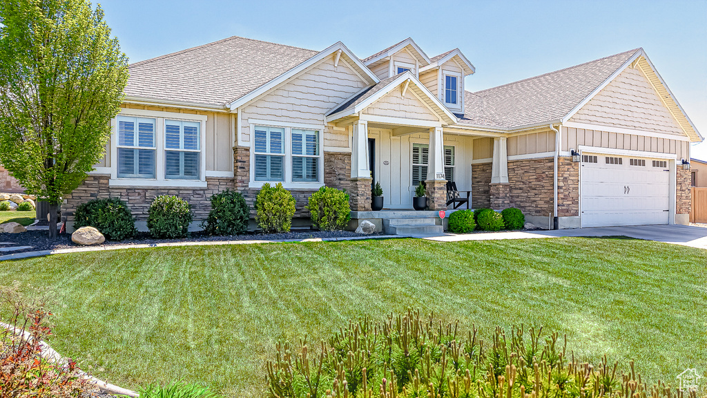Craftsman-style home with stone siding, board and batten siding, an attached garage, and a front yard