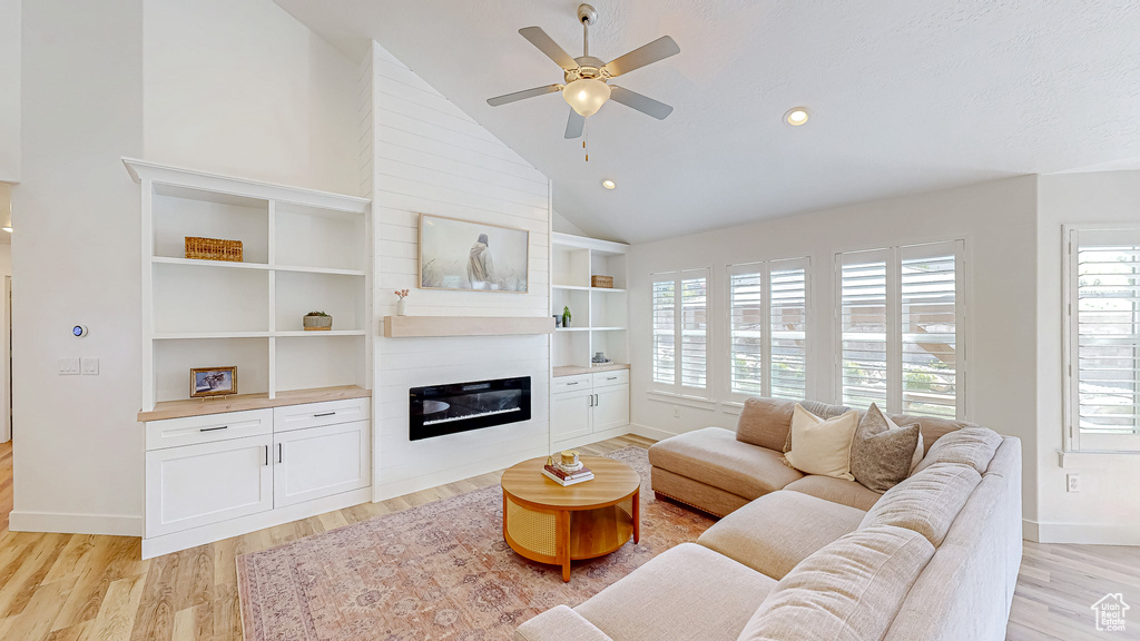 Living room with a glass covered fireplace, light wood-style flooring, a ceiling fan, high vaulted ceiling, and baseboards