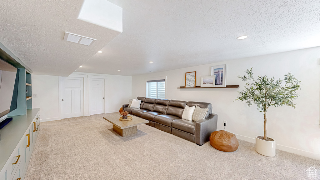 Living area with light colored carpet, a textured ceiling, recessed lighting, and baseboards
