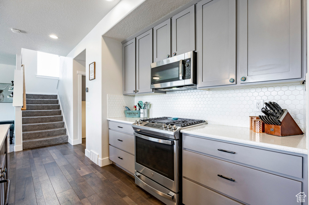 Kitchen with appliances with stainless steel finishes, gray cabinetry, baseboards, light countertops, and recessed lighting