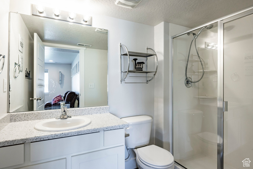 Bathroom with a shower stall, a textured ceiling, toilet, and vanity