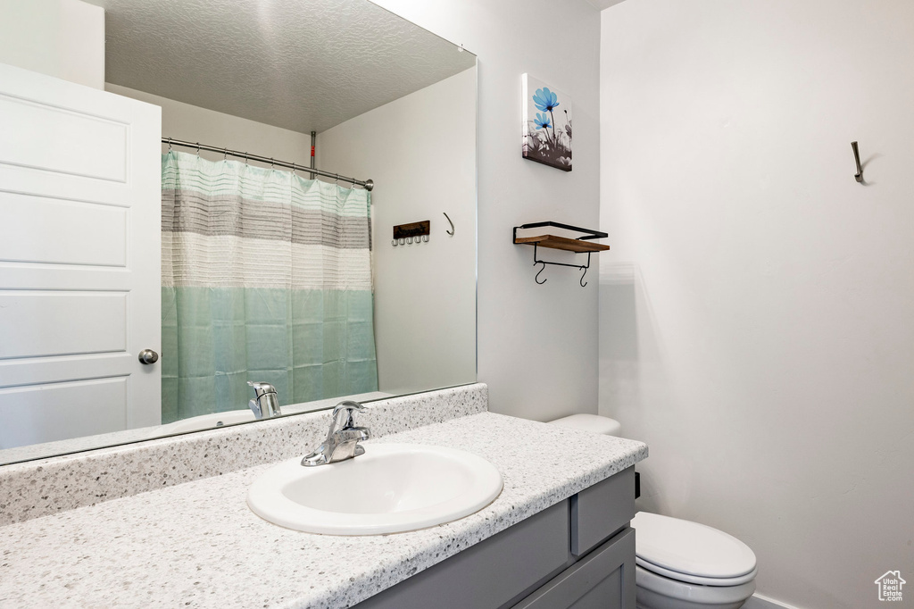 Full bath featuring toilet, vanity, a shower with curtain, and a textured ceiling