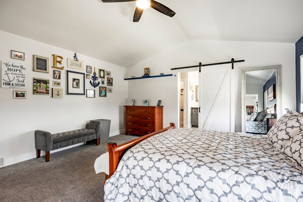 Carpeted bedroom featuring a barn door, vaulted ceiling, baseboards, and a ceiling fan