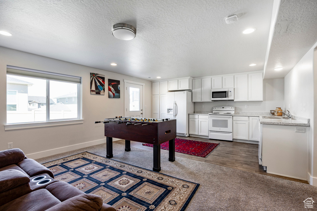 Recreation room featuring a sink, dark carpet, baseboards, healthy amount of natural light, and a textured ceiling