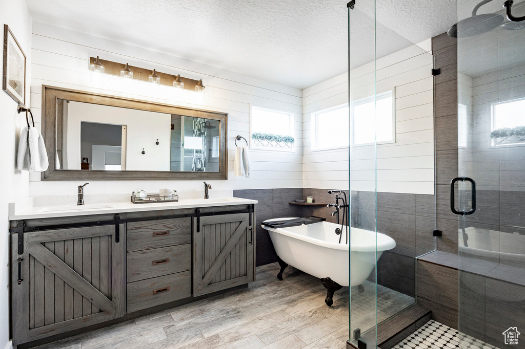 Full bathroom featuring a stall shower, a soaking tub, double vanity, a textured ceiling, and tile walls