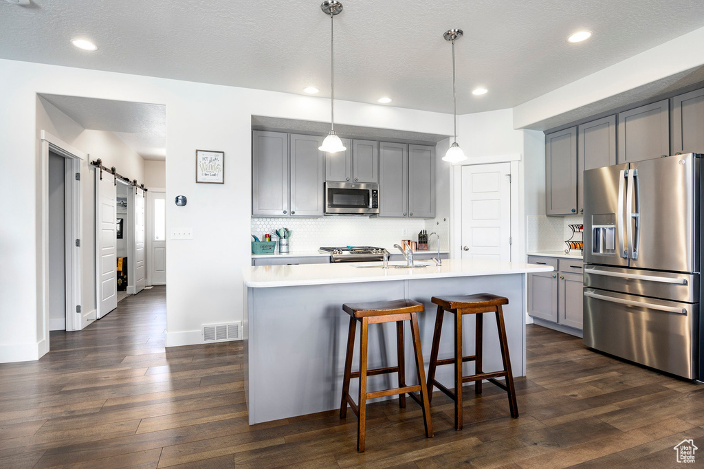 Kitchen featuring appliances with stainless steel finishes, gray cabinets, a sink, light countertops, and decorative backsplash
