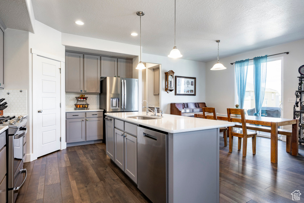 Kitchen featuring gray cabinets, appliances with stainless steel finishes, a sink, dark wood-style floors, and light countertops
