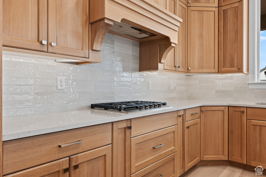 Kitchen with stainless steel gas stovetop, decorative backsplash, custom exhaust hood, and light wood-style flooring