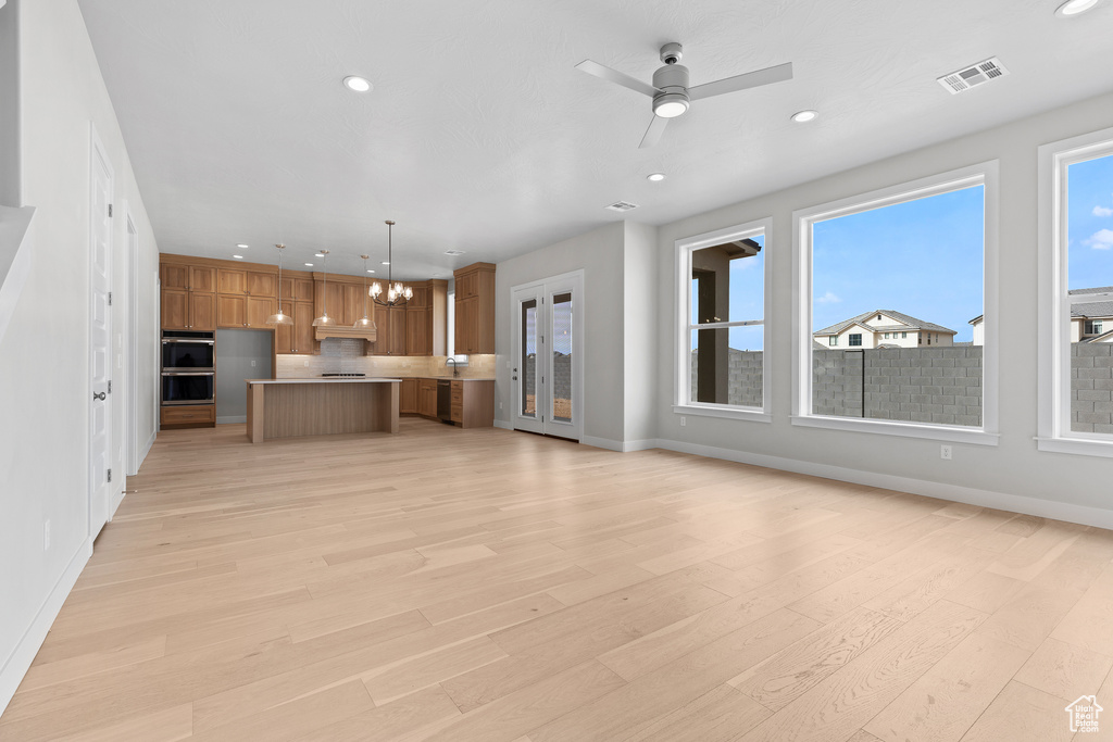 Unfurnished living room featuring a chandelier, recessed lighting, baseboards, light wood-style flooring, and a ceiling fan