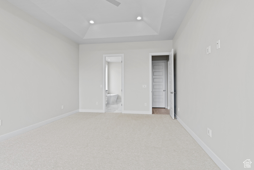 Unfurnished bedroom with recessed lighting, a tray ceiling, light carpet, connected bathroom, and baseboards