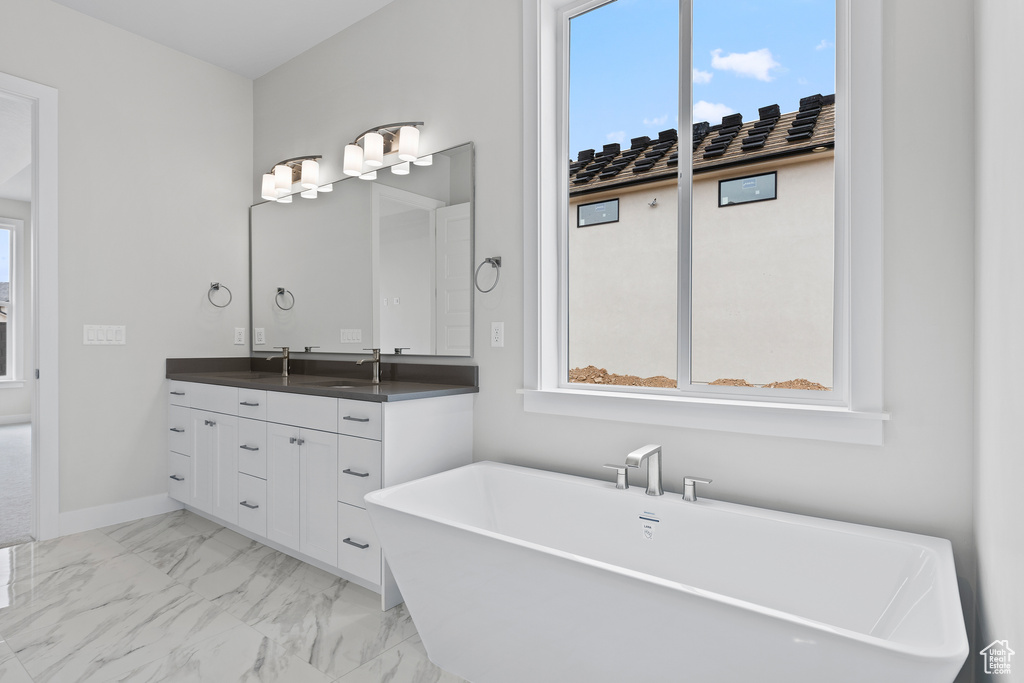 Bathroom featuring marble finish flooring, double vanity, a freestanding tub, and baseboards