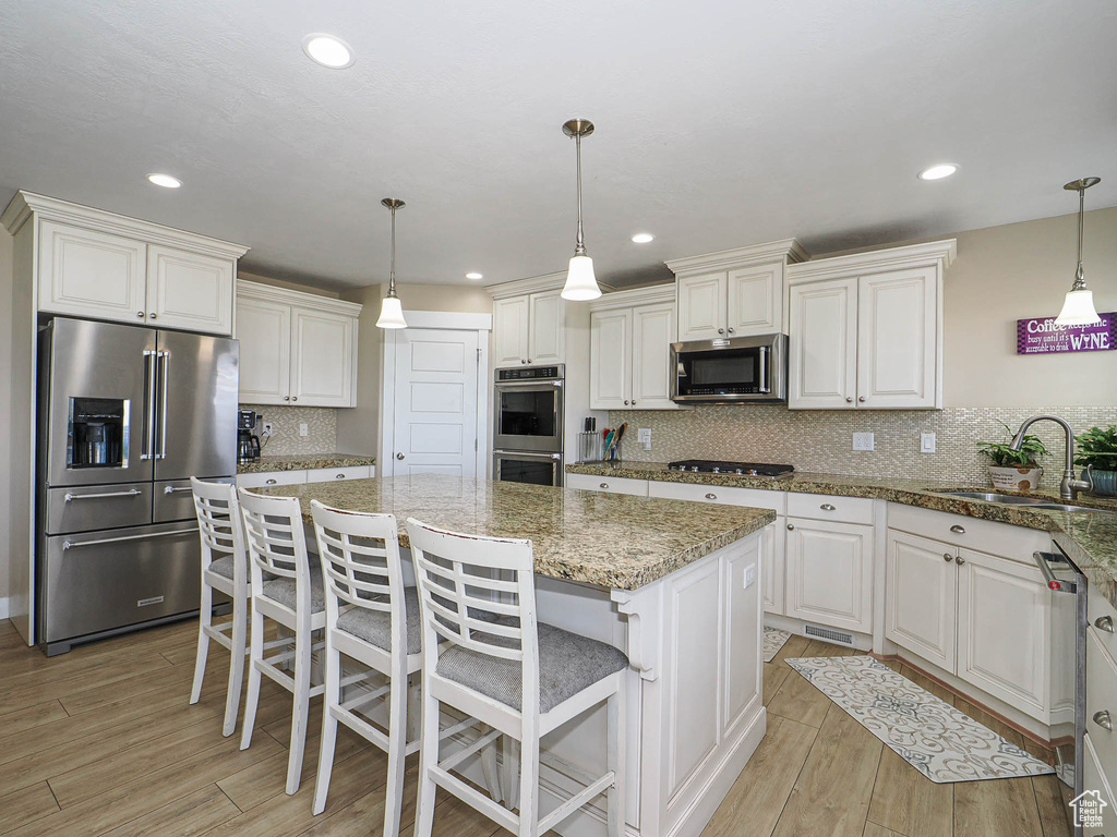 Kitchen featuring stainless steel appliances, a sink, a kitchen island, light wood-type flooring, and backsplash